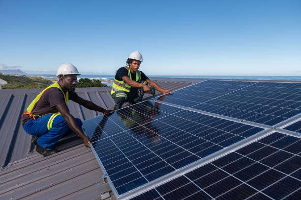 Two African men install solar panels neatly on a residential roof of a house near the ocean. Sustainable living.